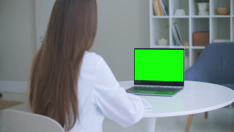 Medical-worker-a-woman-in-a-white-coat-uses-a-tablet-in-the-office-at-the-Desk-chromakey-on-the-tablet-screen-a-view-over-her-shoulder.-doctor-talking-to-laptop-with-green-screen.